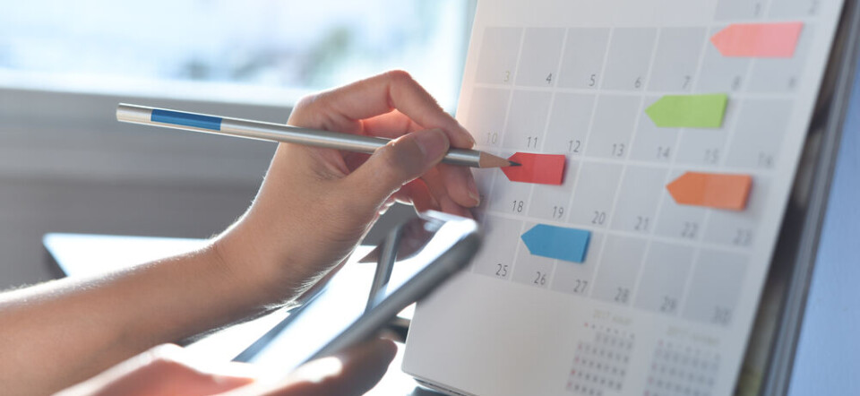 Hand marking a wall calendar while holding a smartphone.